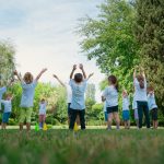 Group of children with instructor doing exercises in a sunny park setting, promoting outdoor activity.
